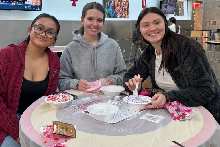 Three students pose at a table while making bath bombs in the Campus Center TV Lounge. 