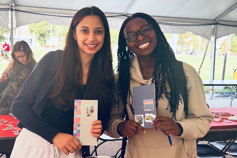 Two students pose showing off artwork at an outdoor event. 